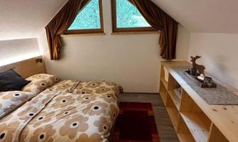A cozy bedroom with a double bed and wooden shelves. The windows let in plenty of light and offer a view of the greenery.