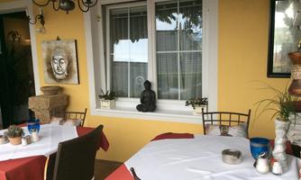 A cozy outdoor area with tables and chairs. The walls are painted yellow and decorated with plants and a Buddha statue.