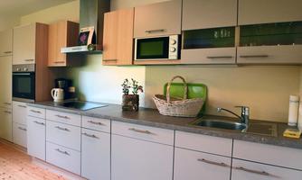 A modern kitchen with light cabinets and a gray workspace. On the countertop, there is a plant and a basket.