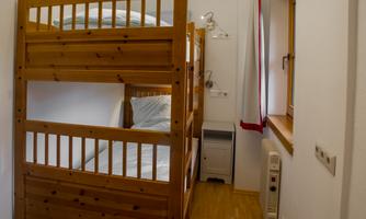 A cozy room with a wooden loft bed and a windowsill. The walls are light, and the floor is wooden.