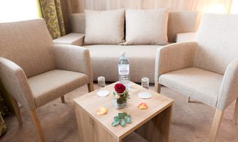 A cozy seating area with two chairs and a couch. On the table, there are water, a rose, and some decorative elements.