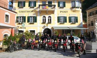 A group of motorcyclists stands in front of the Post Inn. They are wearing black clothing and their motorcycles are decorated with flags.