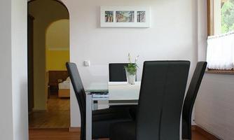 A modern dining area with a white table and black chairs. In the background, an elegant passage and a cozy room are visible.