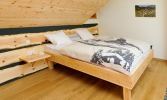 A cozy bedroom with a wooden bed and high-quality bedding. The walls are made of light wood, creating a warm atmosphere.