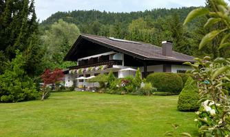 A large house with a green garden and many trees. Gentle hills can be seen in the background.