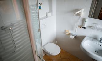 A simple bathroom with a shower, toilet, and sink. The walls are light tiled and the floor is tiled.