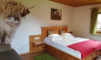 A cozy bedroom with a large bed and wood decor. On the wall, there is a picture of a Highland cow.