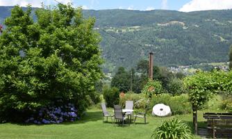 A beautiful garden with a green meadow and colorful flowers. In the background, the mountains and a blue sky are visible.