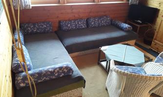 A cozy living area with a large corner sofa and a coffee table. Next to a window, there is a television and rattan chairs.