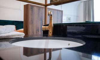 A modern bathroom with an elegant sink and a gold-colored faucet. In the background, wooden cabinets and a cozy space can be seen.