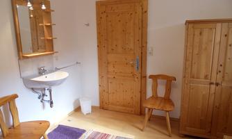 A simple room with a wooden chair and wooden wardrobe. A mirror hangs on the wall above a small sink.
