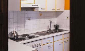A modern kitchen with white cabinets and yellow accents. It is well equipped with a stove, sink, and countertop.