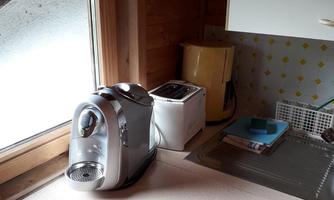 A modern kitchen with a coffee machine and a toaster on the countertop. In the background, there is a window with a view outside.