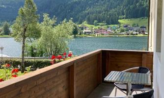 Balcony with a view of a lake and green mountains. Two chairs and a table invite you to relax.