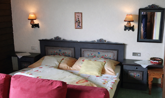 A cozy bedroom with a decorative bed and colorful pillows. Mounted on the walls are wall lamps and a mirror, creating a warm atmosphere.