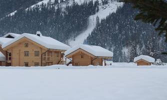 A winter landscape with snow-covered cottages. The mountains in the background are also covered in snow.