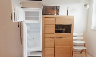 A refrigerator and a kitchen cabinet stand next to each other in a modern kitchen. On the cabinet, there is a microwave and some kitchen utensils.
