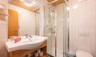 A modern bathroom with a shower, a sink, and a toilet. The walls are tiled and there is a wooden ceiling.
