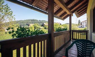 A cozy balcony with a wooden railing that offers a view of green meadows and trees. The sun is shining and creates an inviting atmosphere.