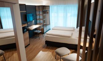 A modern hotel room with two single beds and a desk. Large windows let in plenty of light and create a bright atmosphere.