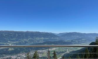 A stunning mountain landscape with a clear blue sky. In the foreground, there is a railing that offers a view of the valley and the surrounding hills.