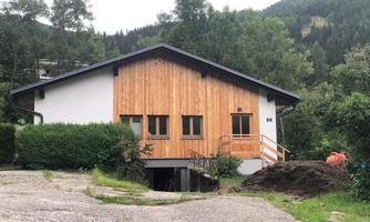 A modern house with wooden cladding and large windows. Surrounded by green nature and trees.