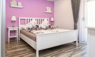A bright bedroom with a white bed and purple walls. The furnishings include nightstands and curtains that create a cozy atmosphere.