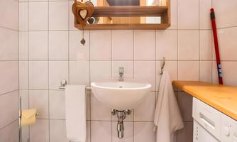 A small bathroom with tiled walls. There is a sink, a large mirror, and a washing machine.