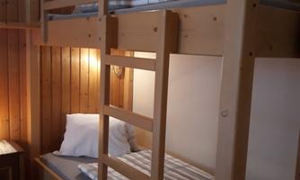 A cozy room with a wooden bunk bed. The walls are made of wood and the lighting is soft.