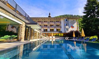 A modern hotel with an inviting pool and green loungers. In the background, trees and a clear blue sky can be seen.