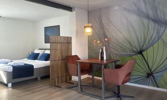 A modern room with a cozy bed and a dining table. The wall is decorated with a beautiful plant motif.