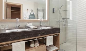A modern bathroom with two sinks and wooden shelves. The shower is separated by a glass wall and the design is simple and elegant.