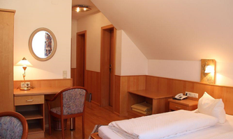A cozy room with wooden decor, a bed, and a small desk. There is also a mirror and a lamp that create a pleasant atmosphere.