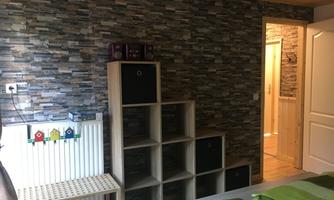 A cozy room with a stone wall and a modern shelf. In the background, access to another room is visible.