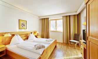 A cozy bedroom with two single beds and wooden furniture. Large windows provide plenty of daylight and a welcoming atmosphere.