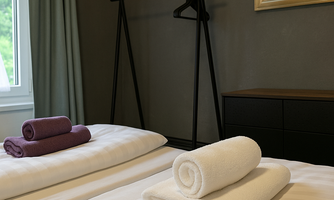 A cozy bedroom with two beds, each with fresh towels. A clothing rack and a mirror enhance the tranquil atmosphere.