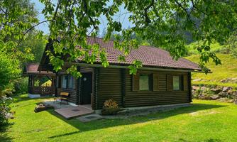 A cozy wooden house surrounded by green grass and trees. The serene landscape creates an inviting atmosphere.