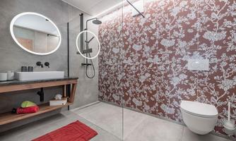 A modern bathroom with a spacious shower and a flower-adorned wall. In the foreground, there is a wooden vanity with a mirror and colorful towels.
