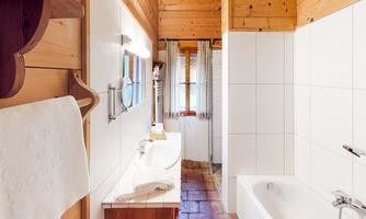 A cozy bathroom with wooden walls and tiled floors. There is a sink, a bathtub, and large windows for natural light.