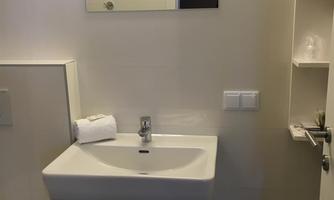 A modern bathroom with a white sink, a large mirror, and minimalist design. The walls are light, and there is a towel on the sink.