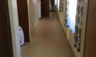 A bright hallway with walls in neutral tones.  
On the wall, there are wardrobe lockers and large windows with curtains.