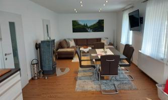 A modern living room with a large dining table and comfortable sofas. On the wall hangs a television and a landscape painting.