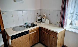 A small kitchen with a sink and wooden kitchen cabinets. On the countertop, there is a kettle and a coffee machine.
