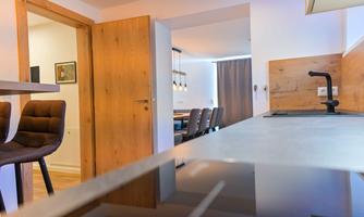 A modern kitchen with barstools and a view of a dining area. The space is bright and inviting with wooden elements and neutral colors.