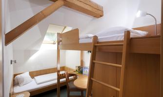 A cozy room with a loft bed and a single bed. There is a small table and wooden chairs.