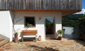 A cozy outdoor area with a stone slab and a bench. In the background, you can see a green landscape and a clear sky.