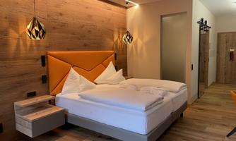A modern bedroom with a large bed and elegant wooden paneling. The warm colors and stylish lamps create a cozy atmosphere.