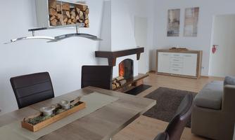 A modern living room with a cozy fireplace and a large dining table. The decor is bright and friendly, with a minimalist design.