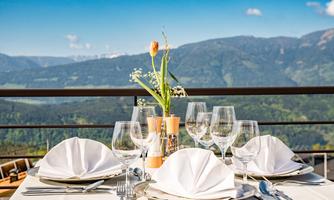 An elegant table for two with starched napkins and wine glasses. In the background, a picturesque mountain landscape stretches under a clear blue sky.