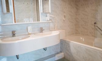 A modern bathroom with a white vanity and two sinks. In the background, there is a bathtub and a mirror.